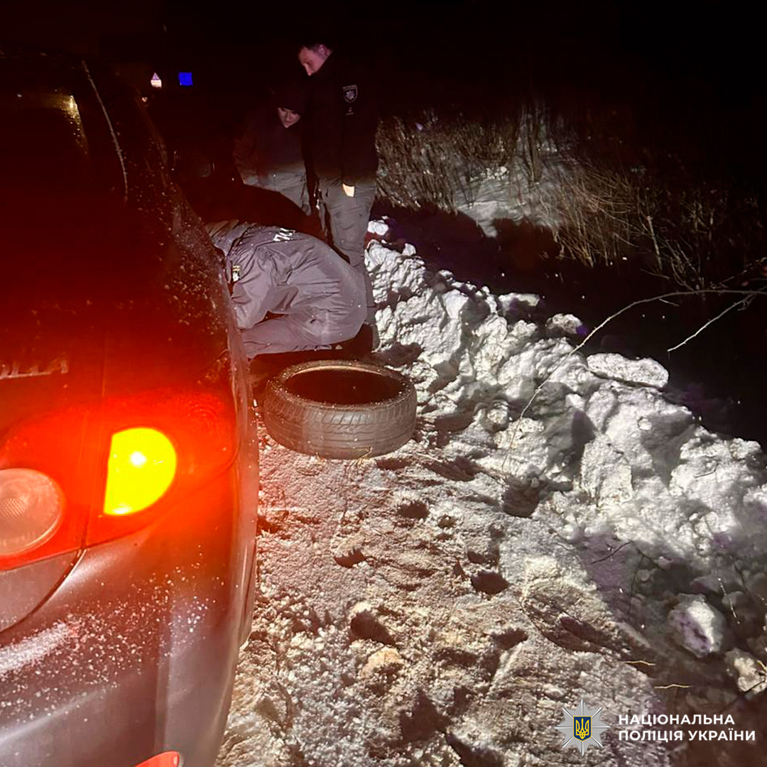 Поліцейські України надають допомогу водієві посеред зимової ночі, працюючи біля автомобіля на снігу.