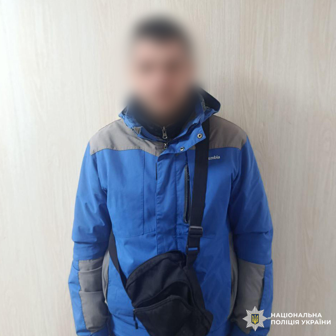 Чоловік у синьо‑сірій зимовій куртці Columbia стоїть біля дерев’яної стіни.