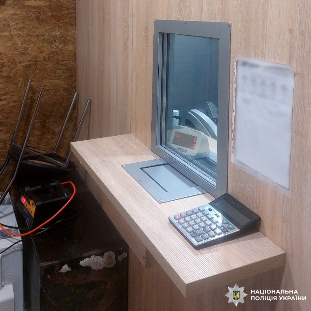 Невелика касова кабінка з дерев’яним прилавком, металевим лотком і калькулятором на столі.