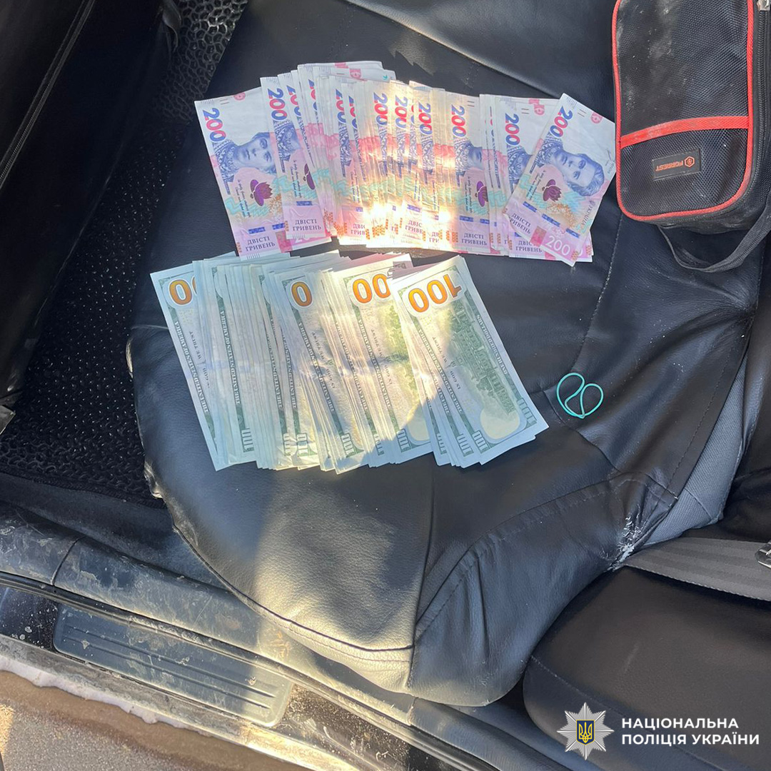 На задньому сидінні авто розкладені 200 гривень і 100 доларів США.