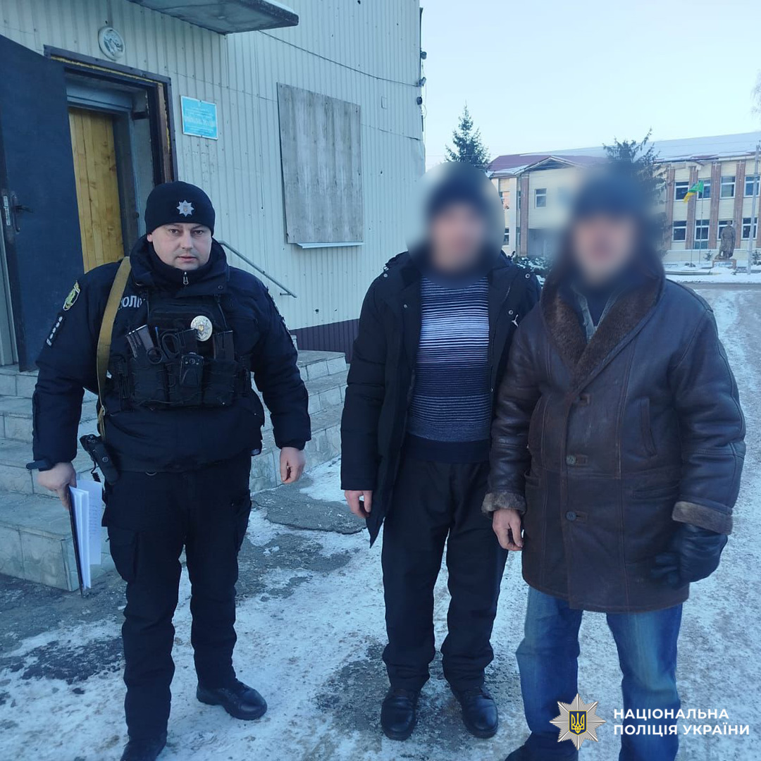 Поліцейський і двоє цивільних стоять біля будівлі на снігу.