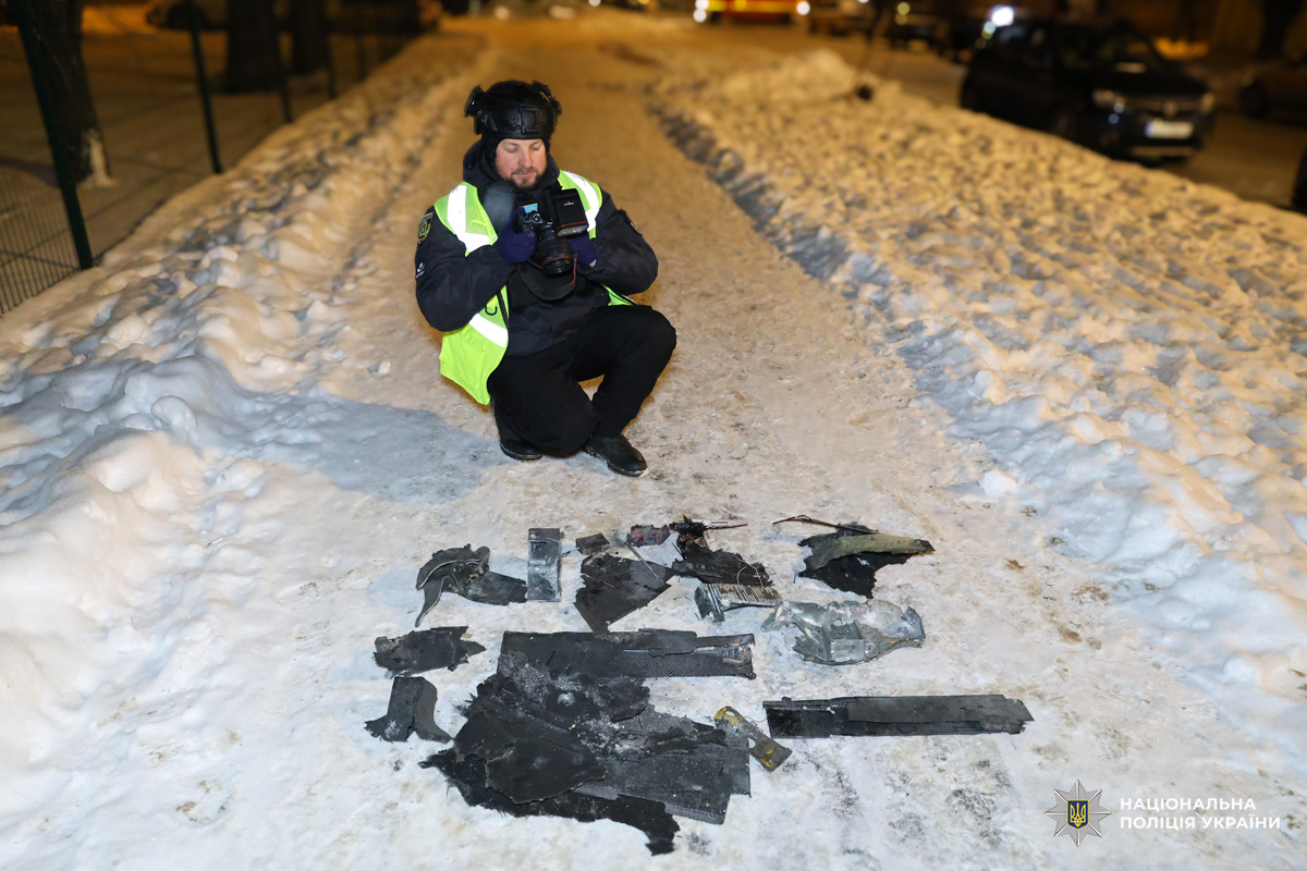 Поліцейський у жилеті фотографує уламки на снігу вночі.