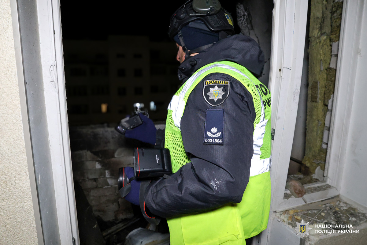 Поліцейський фотографує пошкоджену будівлю вночі.