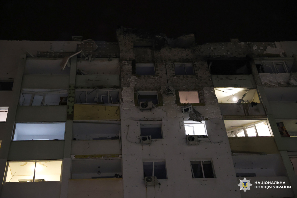 Пошкоджений багатоповерховий будинок уночі, вибиті вікна, сліди обстрілу.