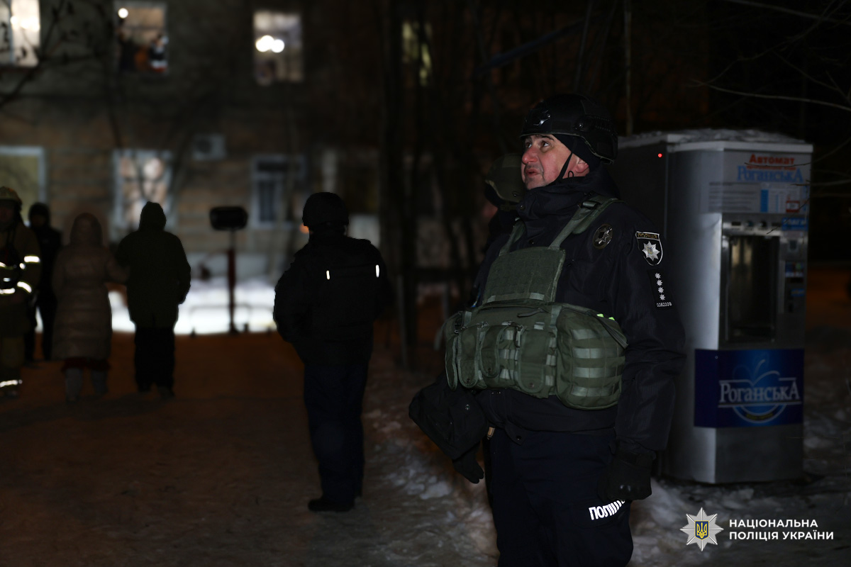Поліцейський у спорядженні стоїть біля будівлі вночі.