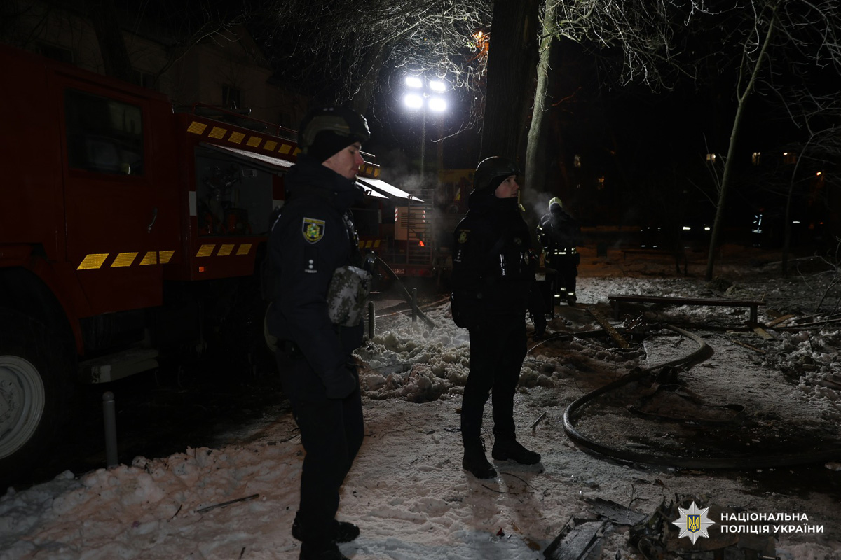 Двоє поліцейських у тактичному спорядженні стоять біля пожежної машини з відкритими відсіками.