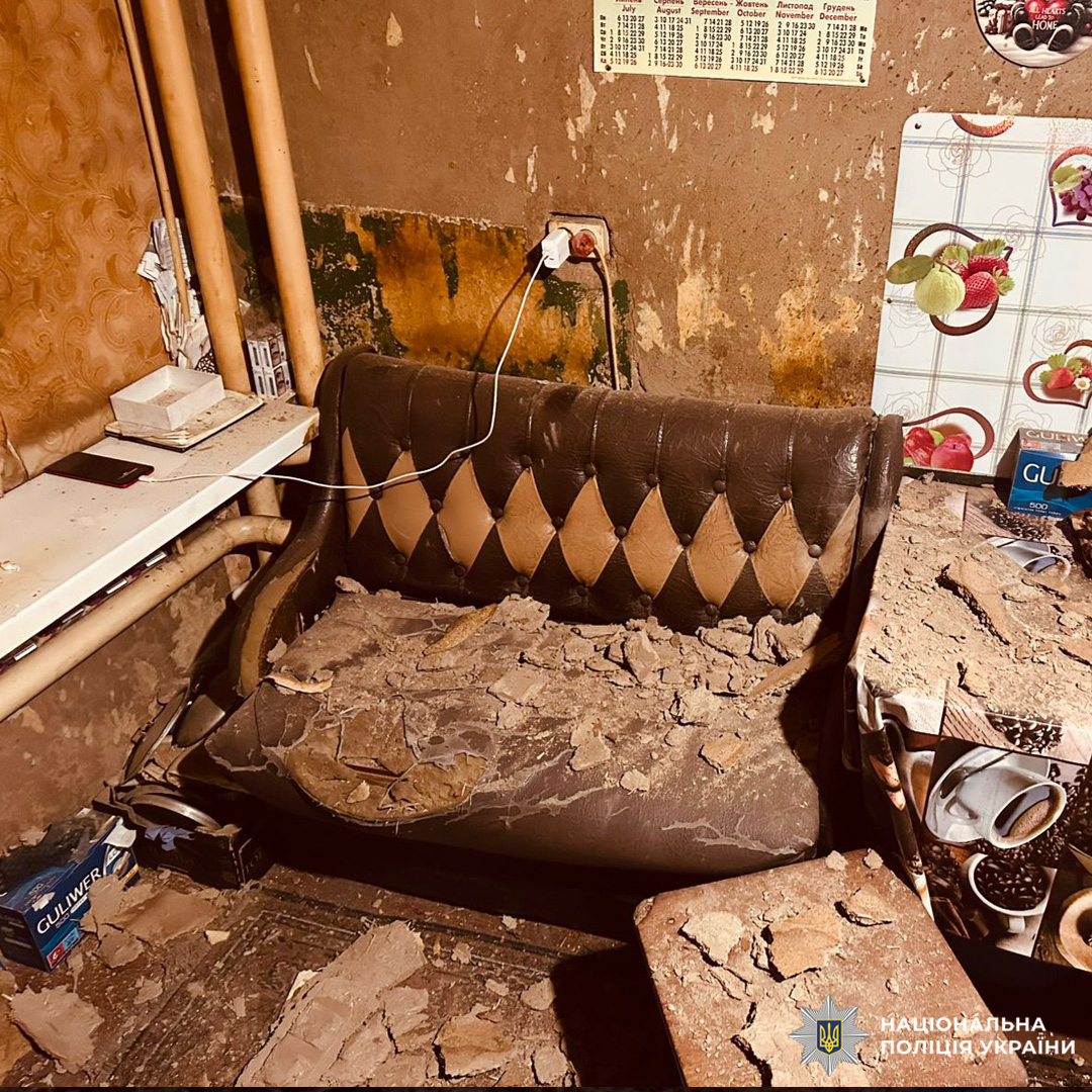 Зруйнована кімната з уламками на меблях.