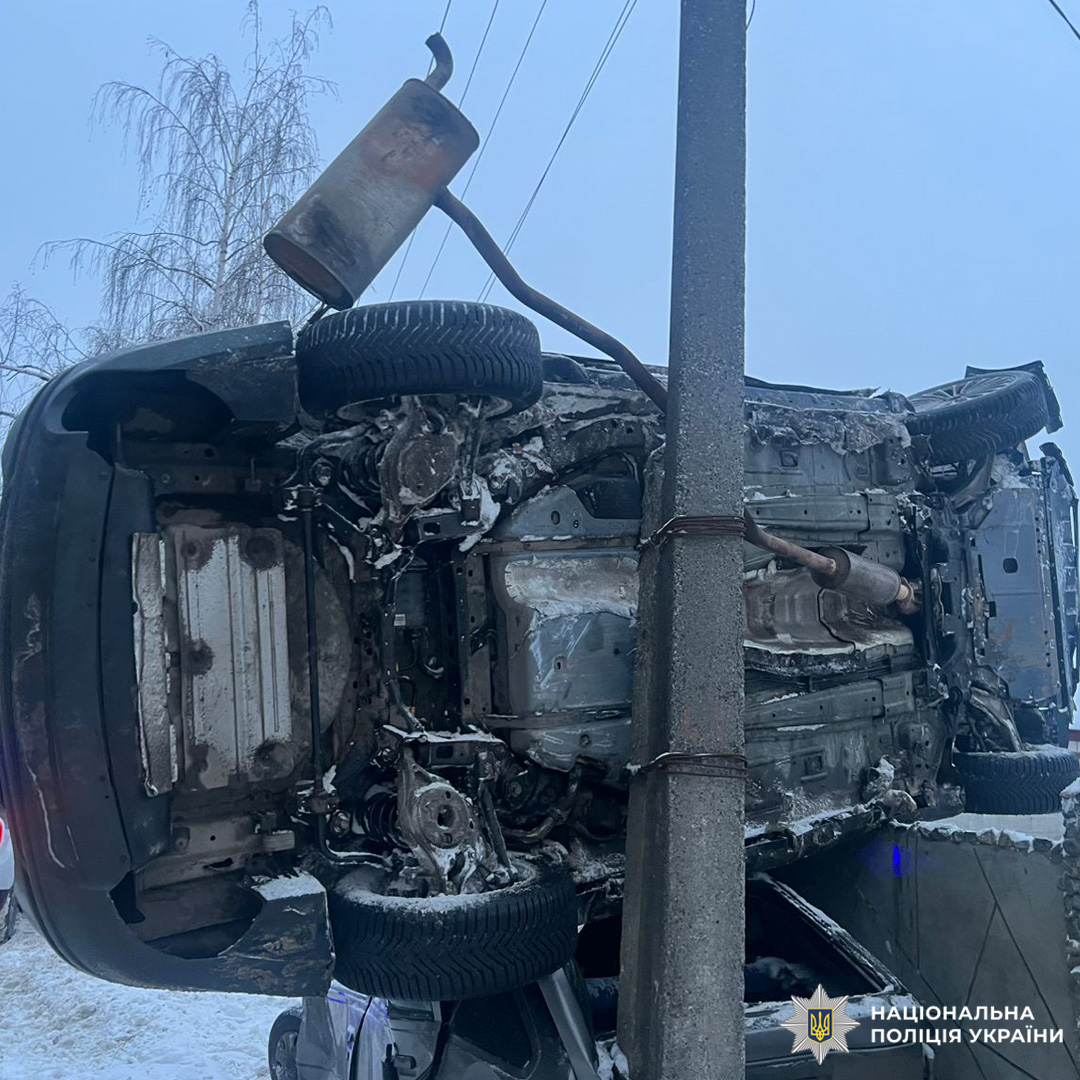 Перевернутий автомобіль лежить на боці біля стовпа.