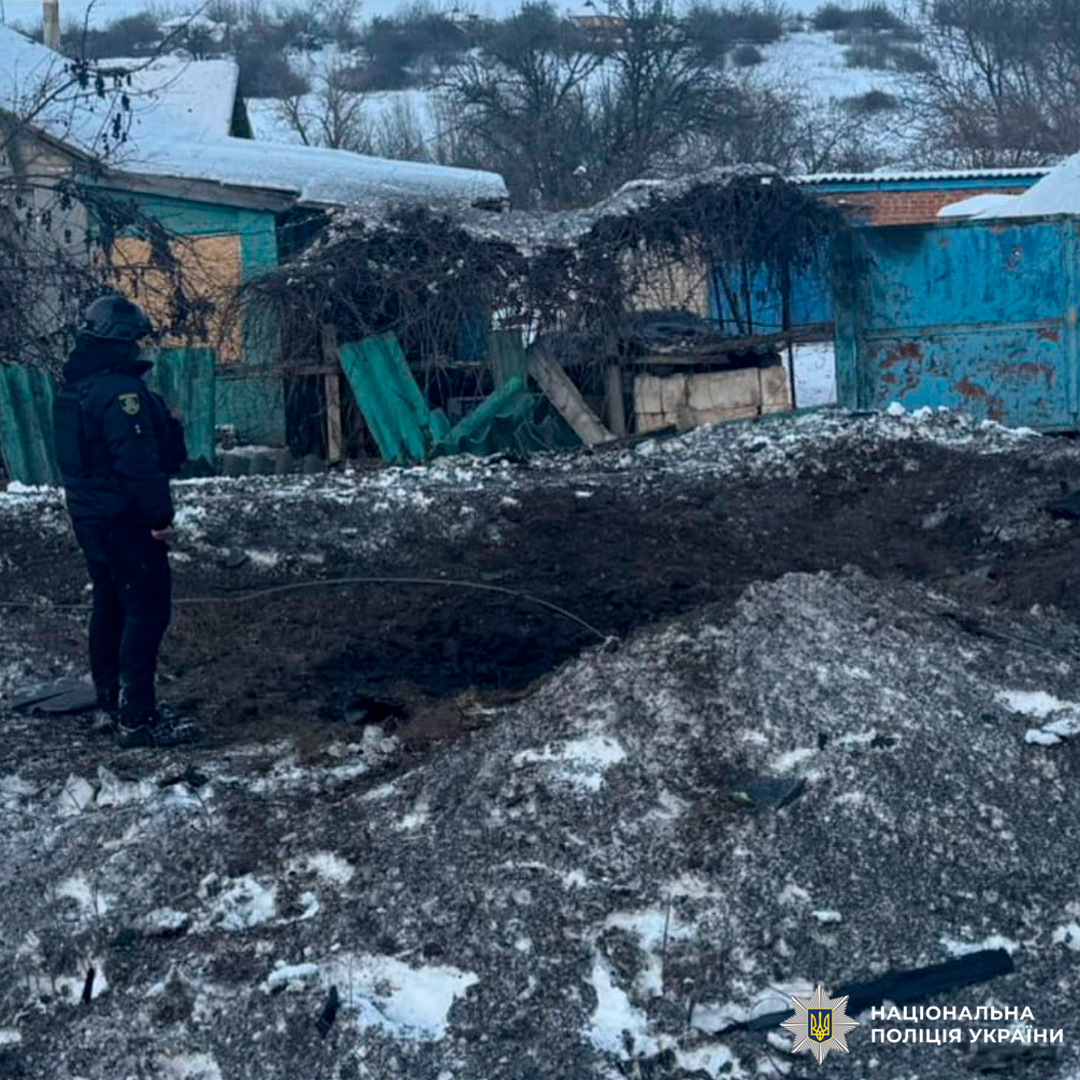 Поліцейський оглядає вирву від вибуху біля пошкоджених будівель у зимових умовах.