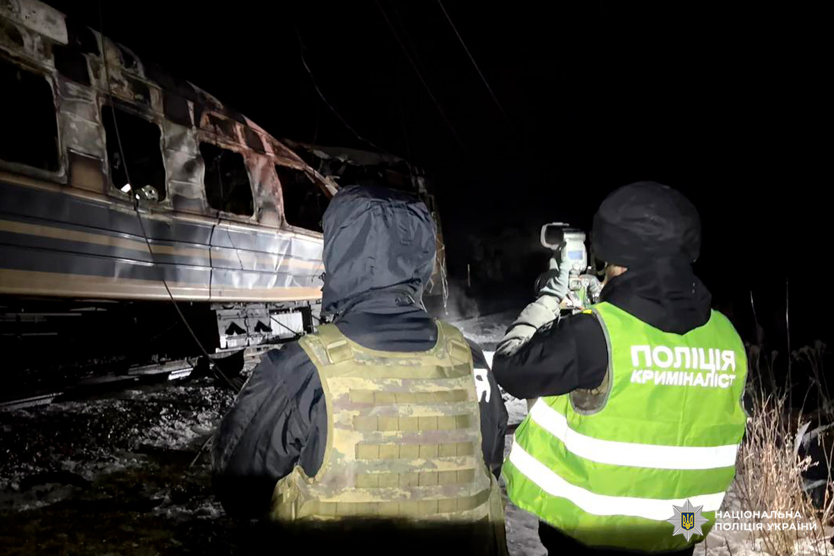Криміналісти поліції оглядають обгорілий вагон поїзда вночі.