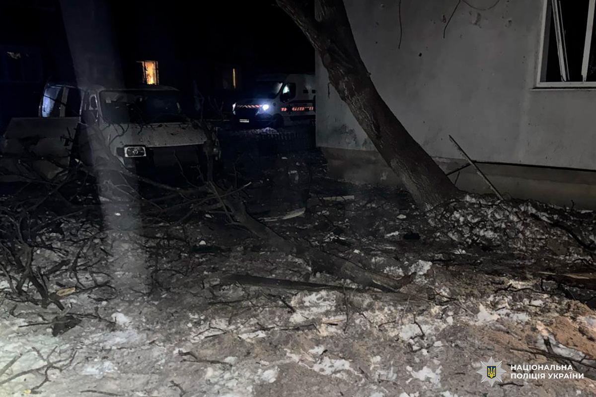 Нічна сцена з руйнуваннями біля будівлі, уламки та пошкоджені автомобілі.