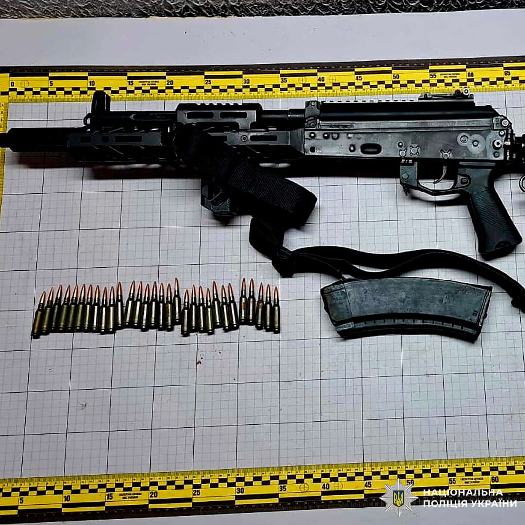 Вилучена тактична гвинтівка чорного кольору з ременем, магазин та 30 набоїв, розташованих на вимірювальній сітці.