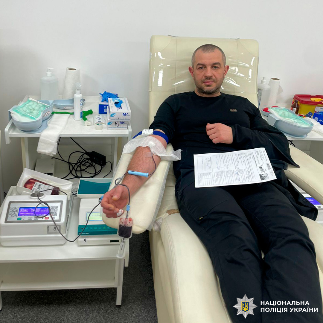 Співробітник Національної поліції України бере участь у процедурі донорства крові. Він перебуває у спеціалізованому медичному закладі, підключений до системи збору крові, поруч із медичним обладнанням та витратними матеріалами.