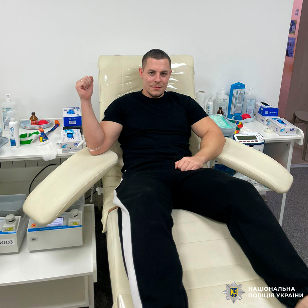 Співробітник Національної поліції України бере участь у процедурі донорства крові. Він перебуває у спеціалізованому медичному закладі, підключений до системи збору крові, поруч із медичним обладнанням та витратними матеріалами.