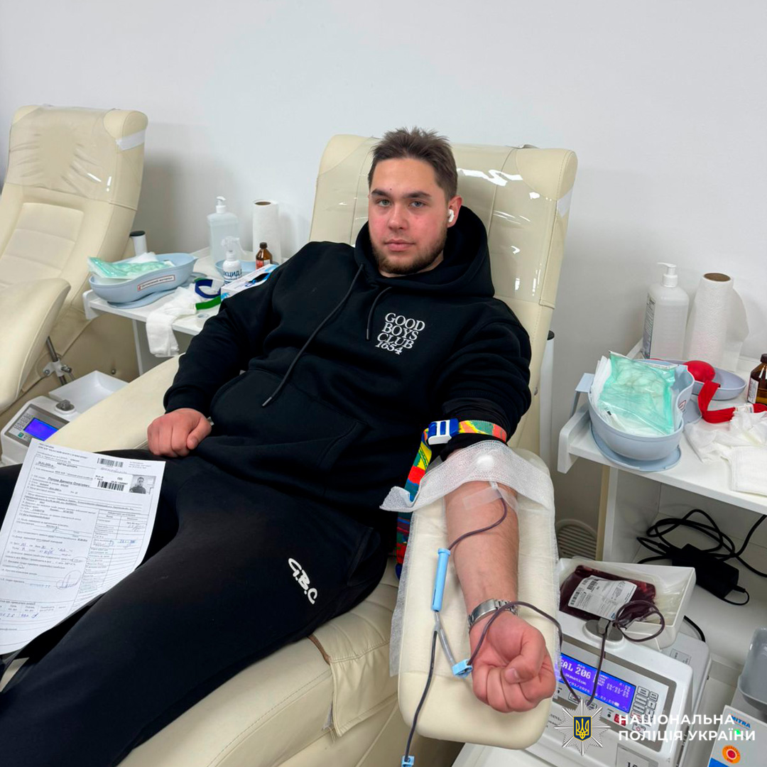 Співробітник Національної поліції України бере участь у процедурі донорства крові. Він перебуває у спеціалізованому медичному закладі, підключений до системи збору крові, поруч із медичним обладнанням та витратними матеріалами.