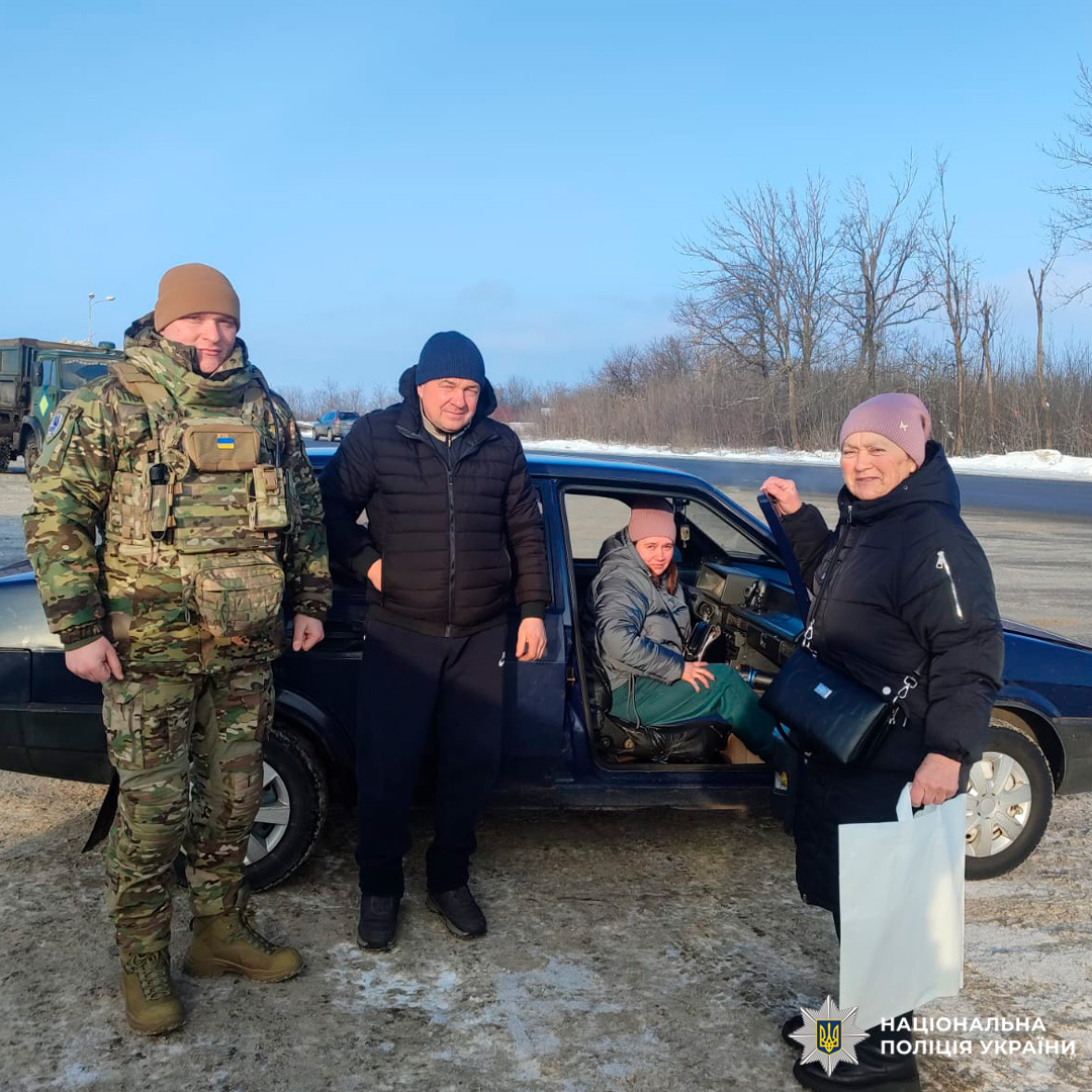 Поліцейський у камуфляжі та цивільні біля автомобіля на засніженій дорозі.