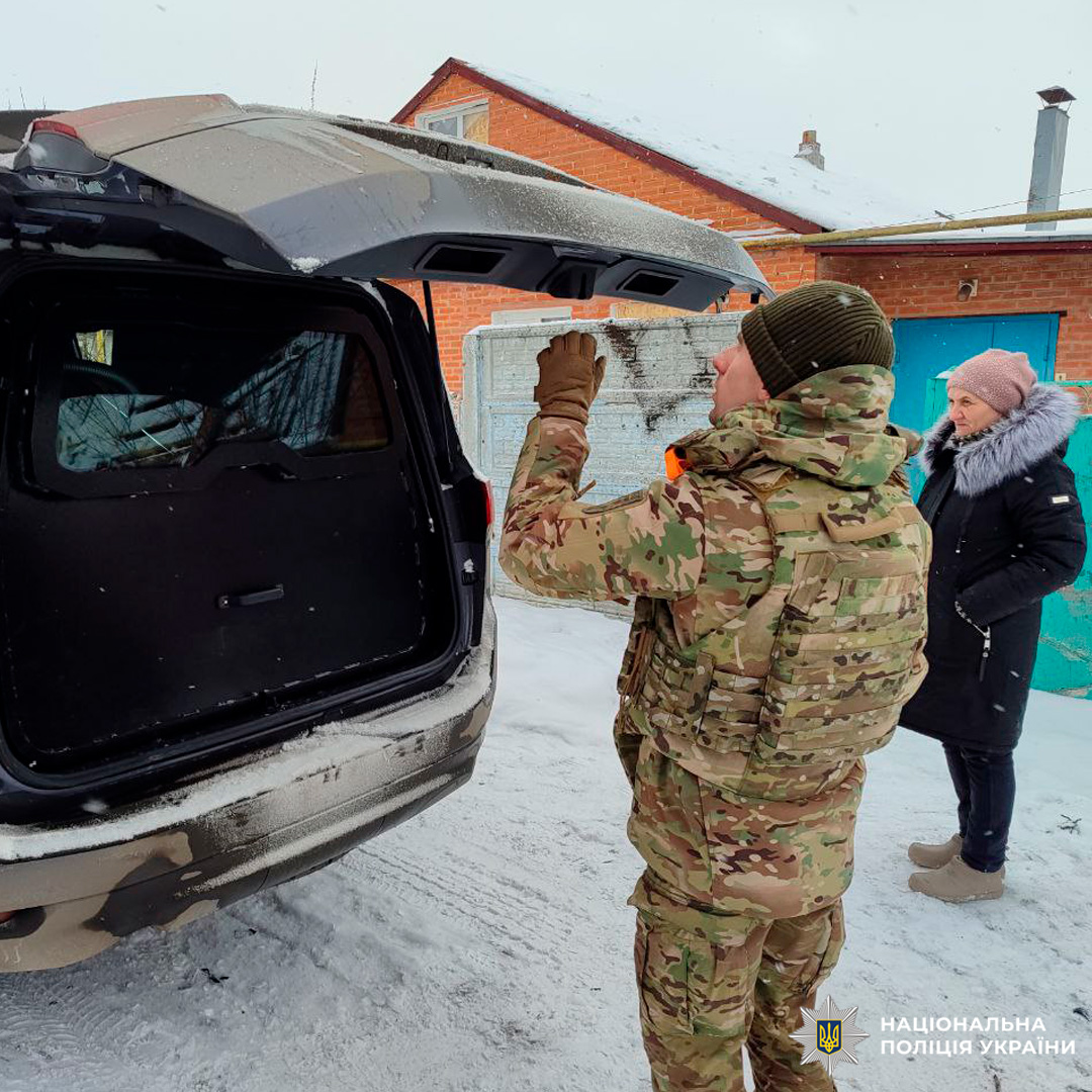 Поліцейський у камуфляжі відкриває багажник автомобіля на засніженому подвір’ї.