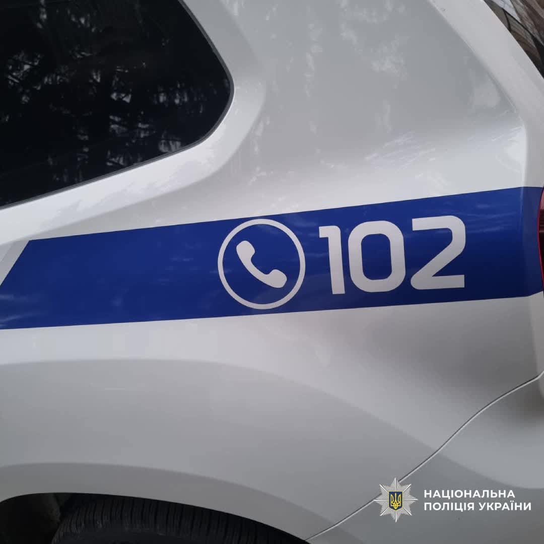 Бокова частина білого поліцейського автомобіля з номером «102» та емблемою Національної поліції України.