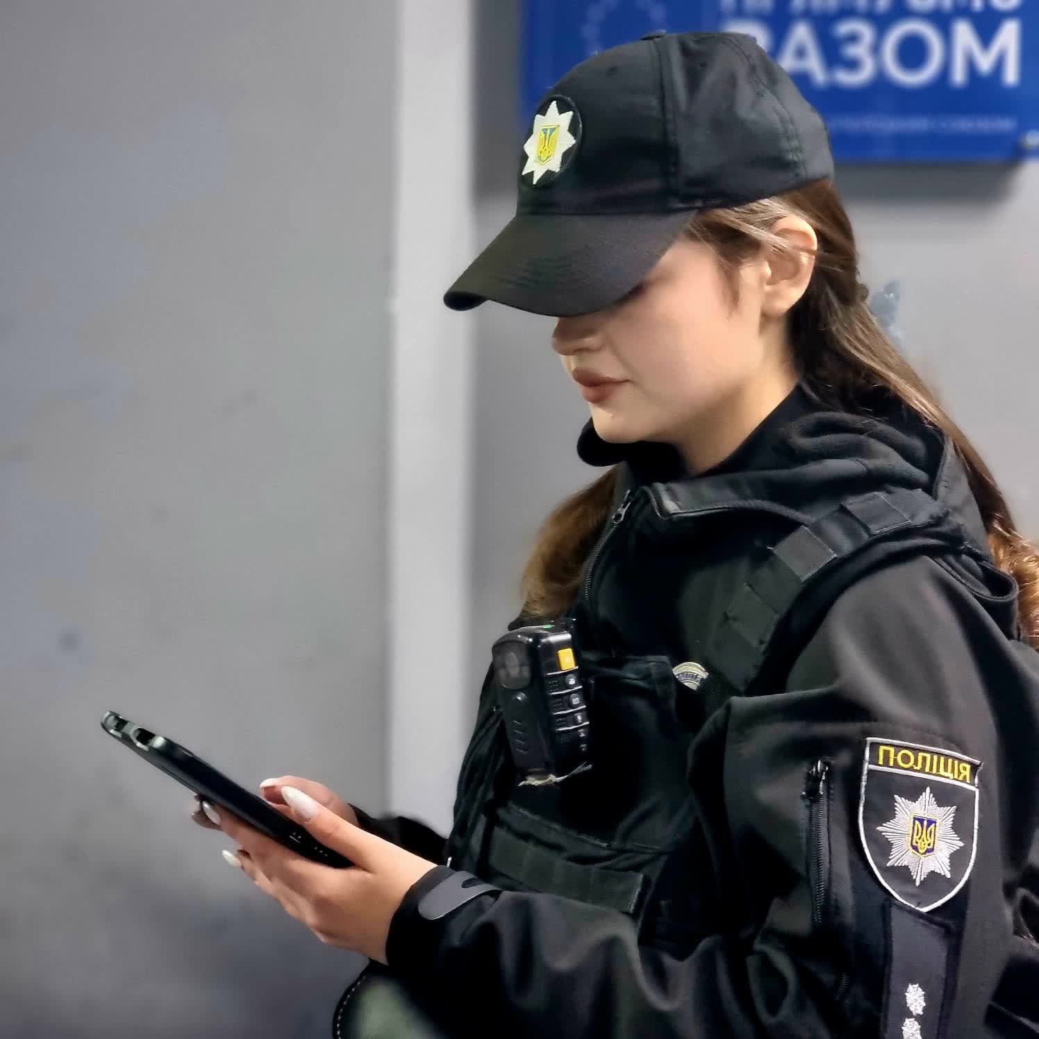 Поліцейський у чорній формі дивиться на смартфон.