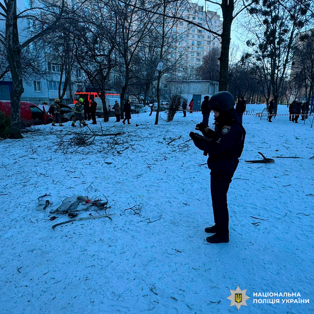 Поліцейський документує уламки на засніженій вулиці, поруч працюють рятувальники та стоять цивільні.