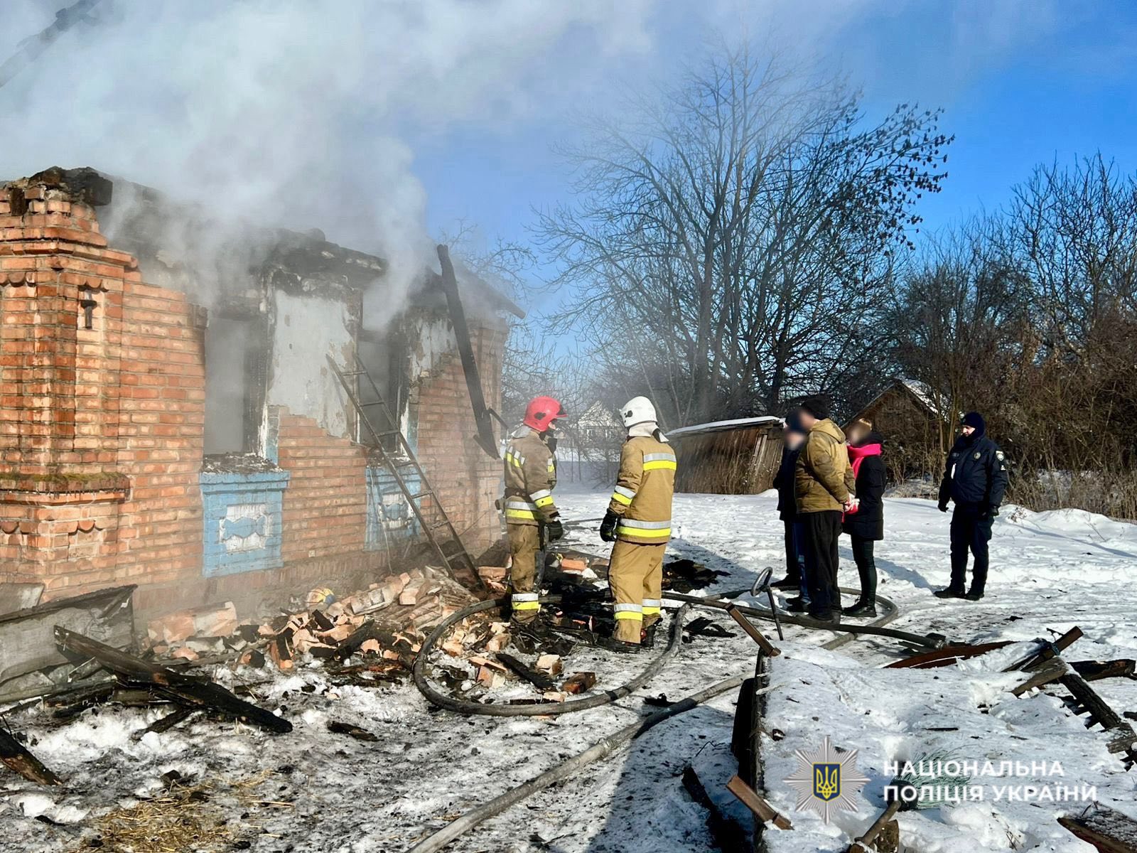 палаючий будинок, який гасять рятувальники. Поблизу люди та поліцейські