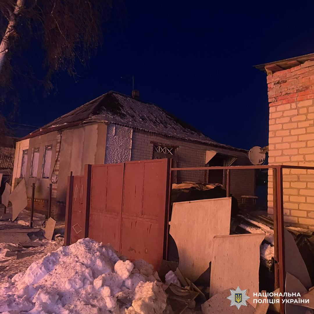 Житлова забудова взимку, сніг на землі, дерева без листя, освітлені будинки та паркан,