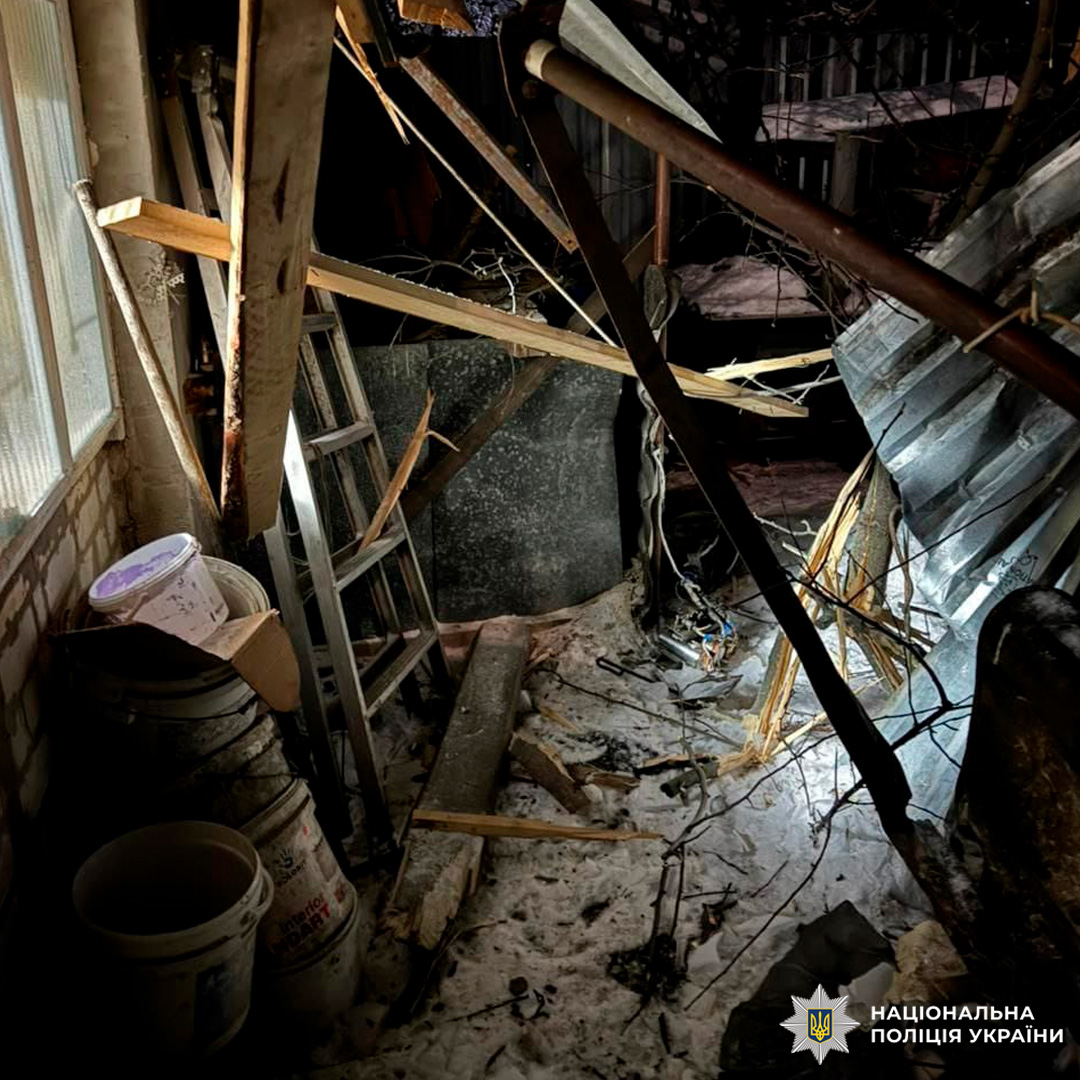 Інтер’єр із руйнуваннями: розбиті балки, зігнутий металевий лист, драбина біля стіни, пластикові відра в кутку, на підлозі сніг і уламки.