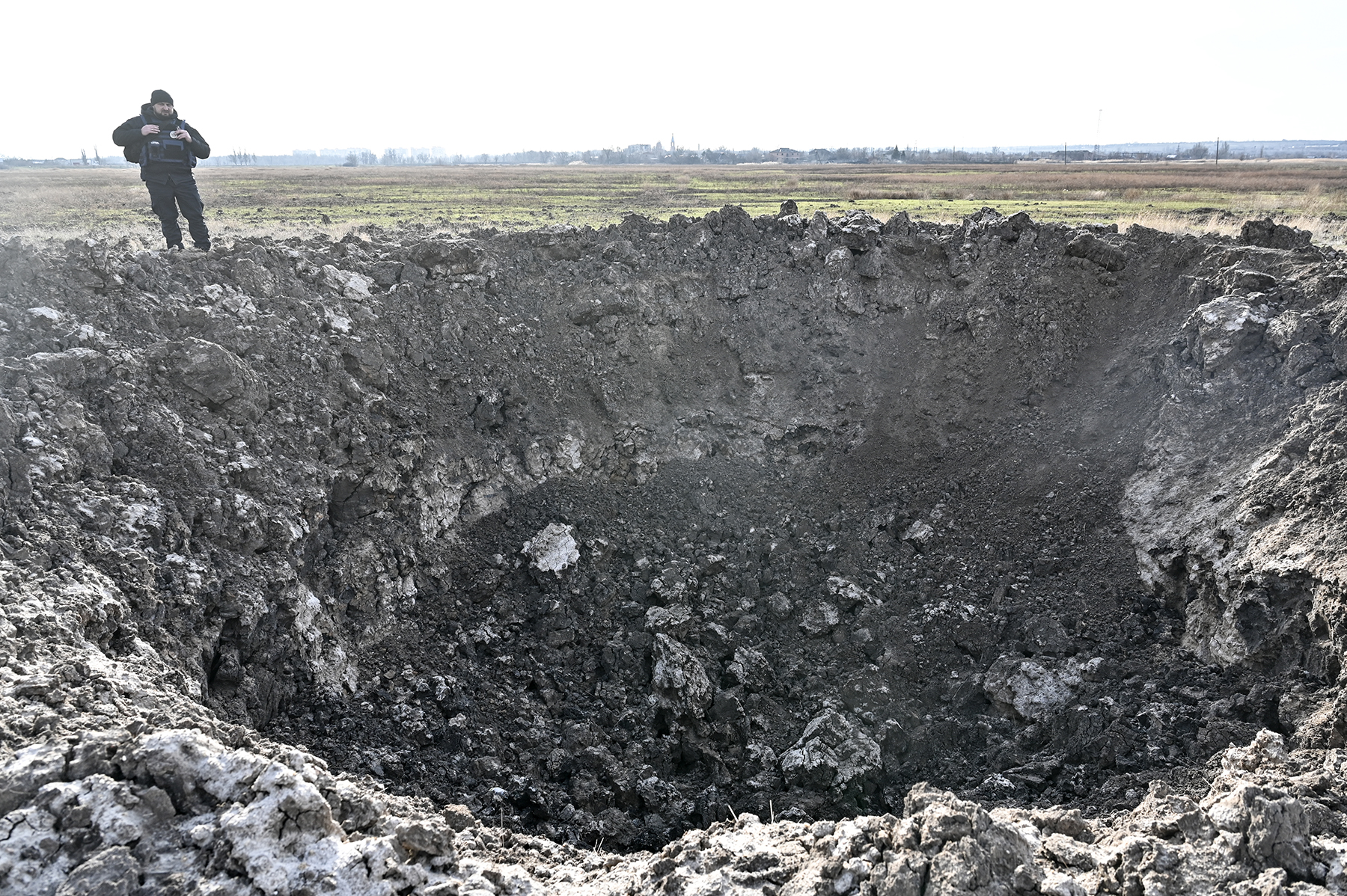 Поліцейський стоїть навпроти вирви від російської авіабомби. Околиці міста Оріхів. Cічень 2025 року.