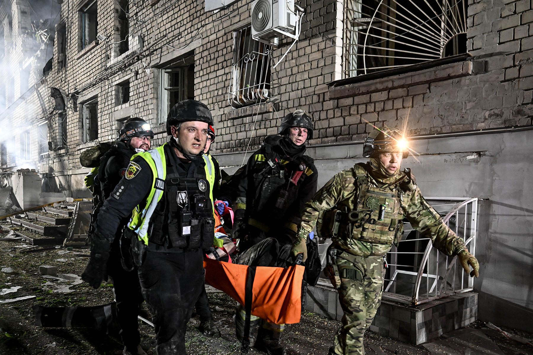 Парамедик запорізької поліції допомагає евакуювати людину, поранену внаслідок ворожого удару по багатоповерхівці в місті Запоріжжя. Травень 2025 року.