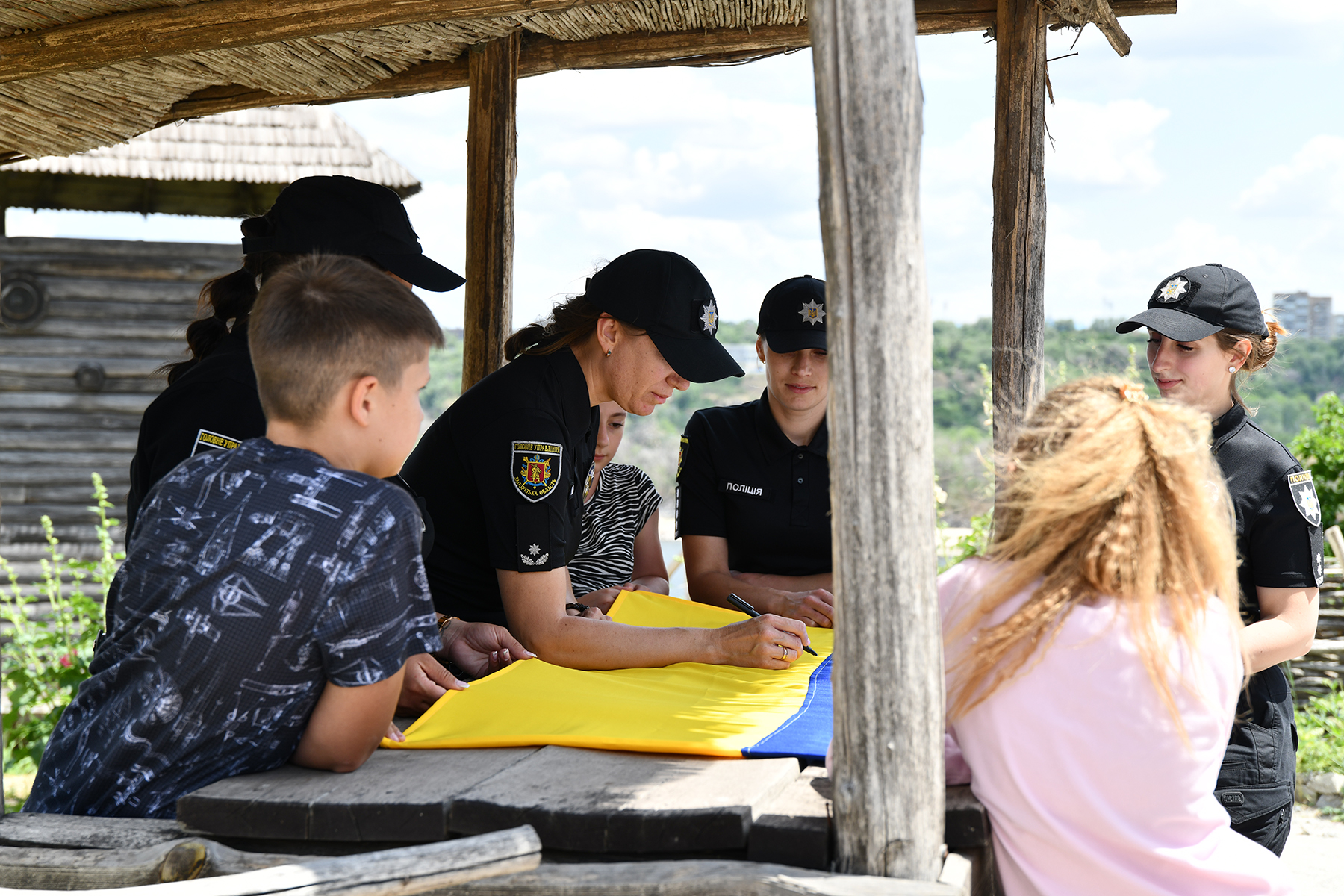 Поліцейські служби освітньої безпеки разом з дітьми підписують прапор на Запорізькій Січі. Липень 2025 року.