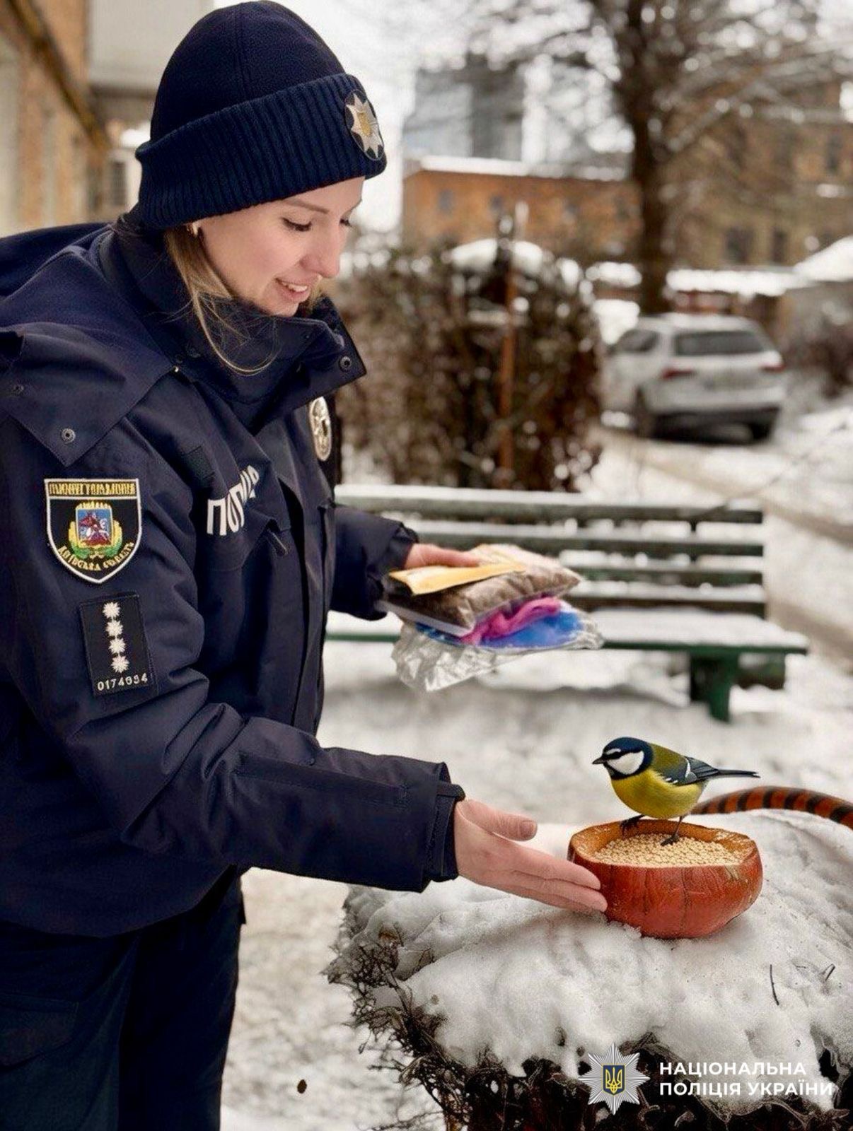 На фото зображена жінка поліцейська, яка годує пташку взимку