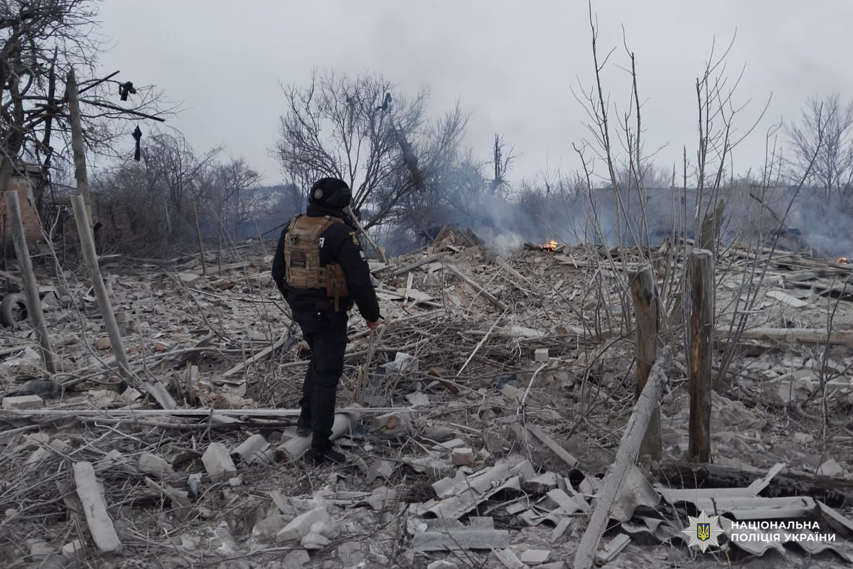 Співробітник Національної поліції України оглядає місце руйнувань після вибуху, серед уламків та диму.