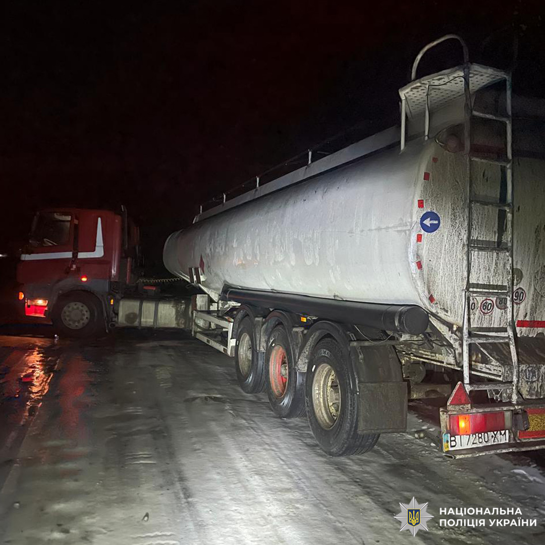 Автоцистерна з червоною кабіною на засніженій дорозі вночі. На задній частині  знаки безпеки та обмеження швидкості.