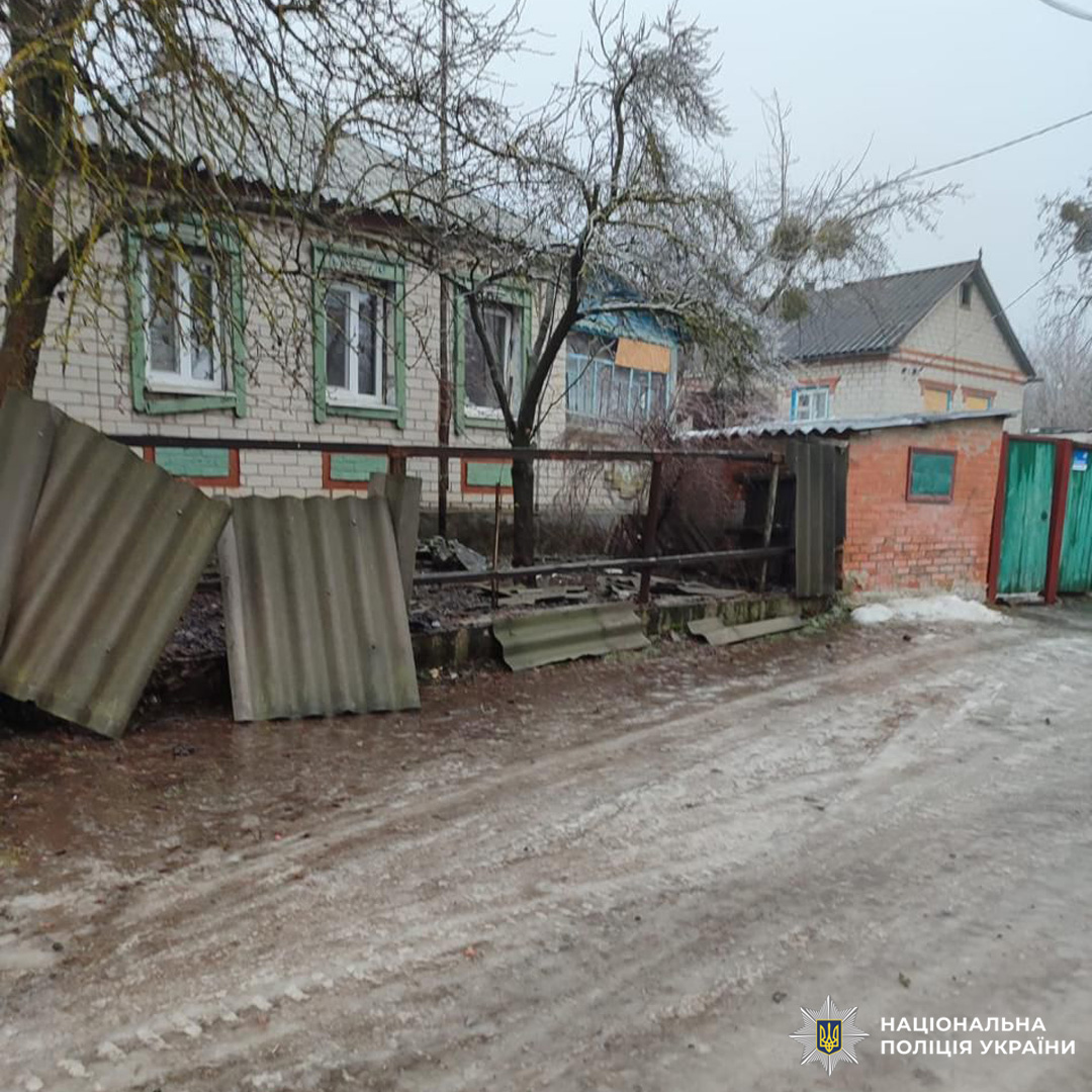 Пошкоджена металева огорожа перед цегляним будинком із зеленими рамами та металевим дахом.