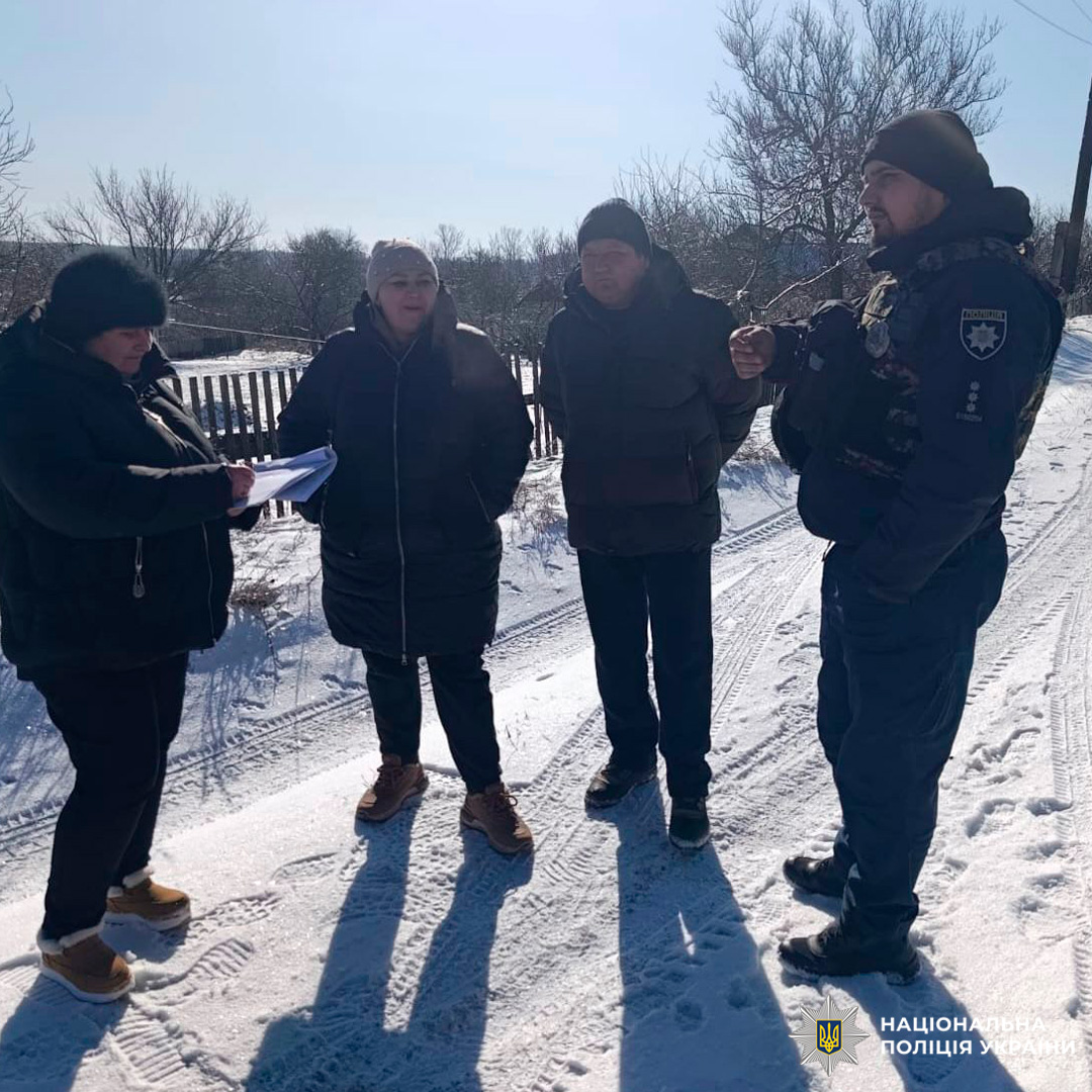 Поліцейський у формі та троє людей у зимовому одязі стоять на засніженій сільській дорозі, один із них робить записи на папері.