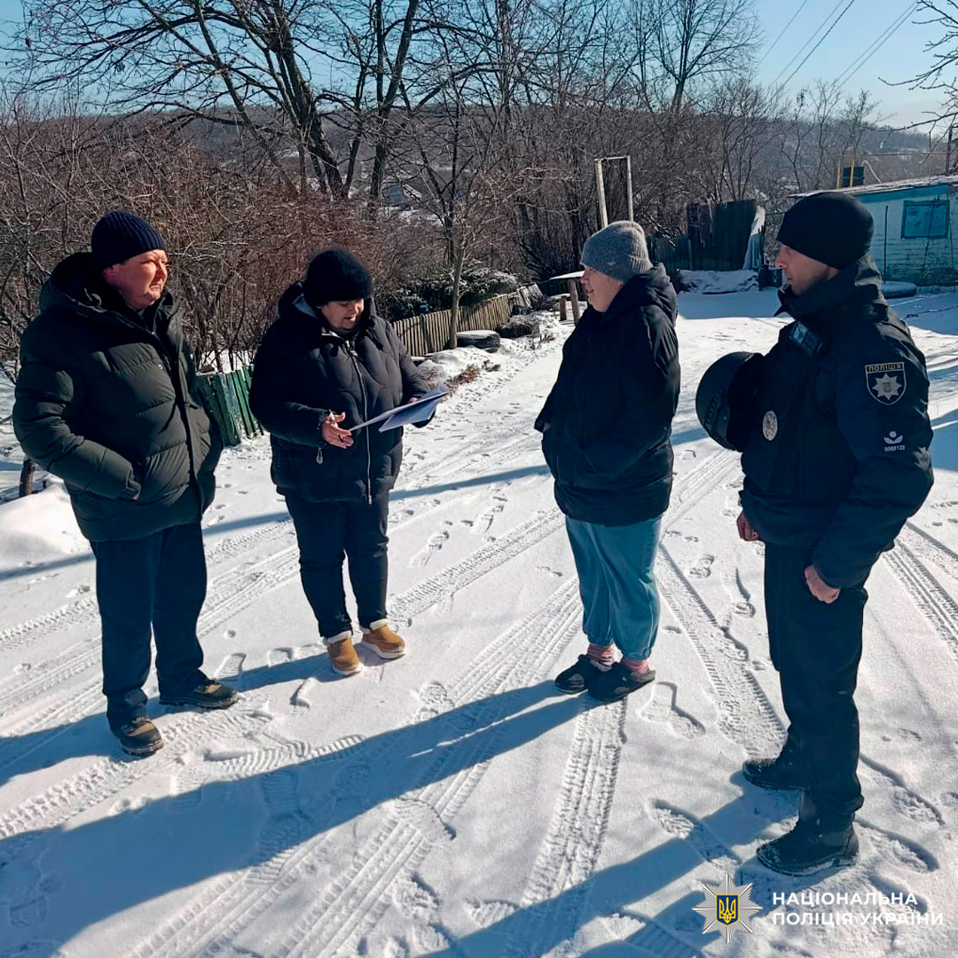 Поліцейський у формі та троє людей у зимовому одязі стоять на засніженій дорозі, один із них тримає папку з документами.