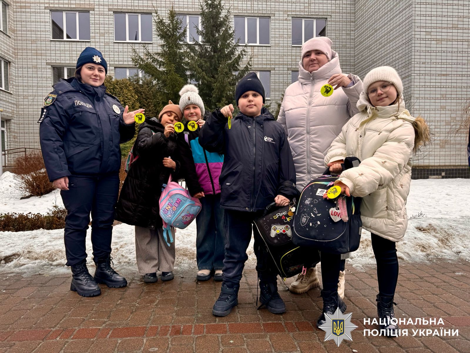 На фотографії зображені поліцейські Київщини, які нагадують учням правила безпечної поведінки та роздають світлоповертальні флікери для того, щоб вони були помітними у темряві.