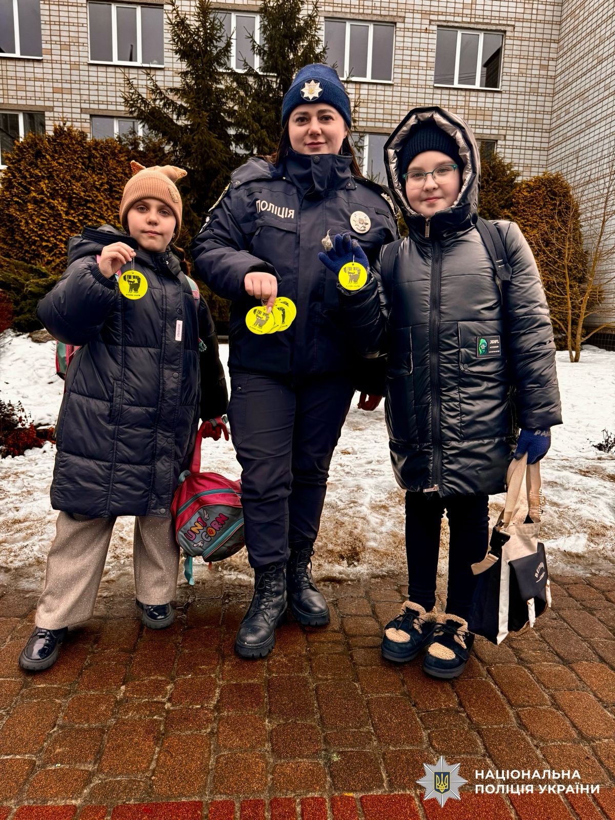 На фотографії зображена поліцейська Київщини, яка нагадує учням правила безпечної поведінки та роздає світлоповертальні флікери для того, щоб вони були помітними у темряві.