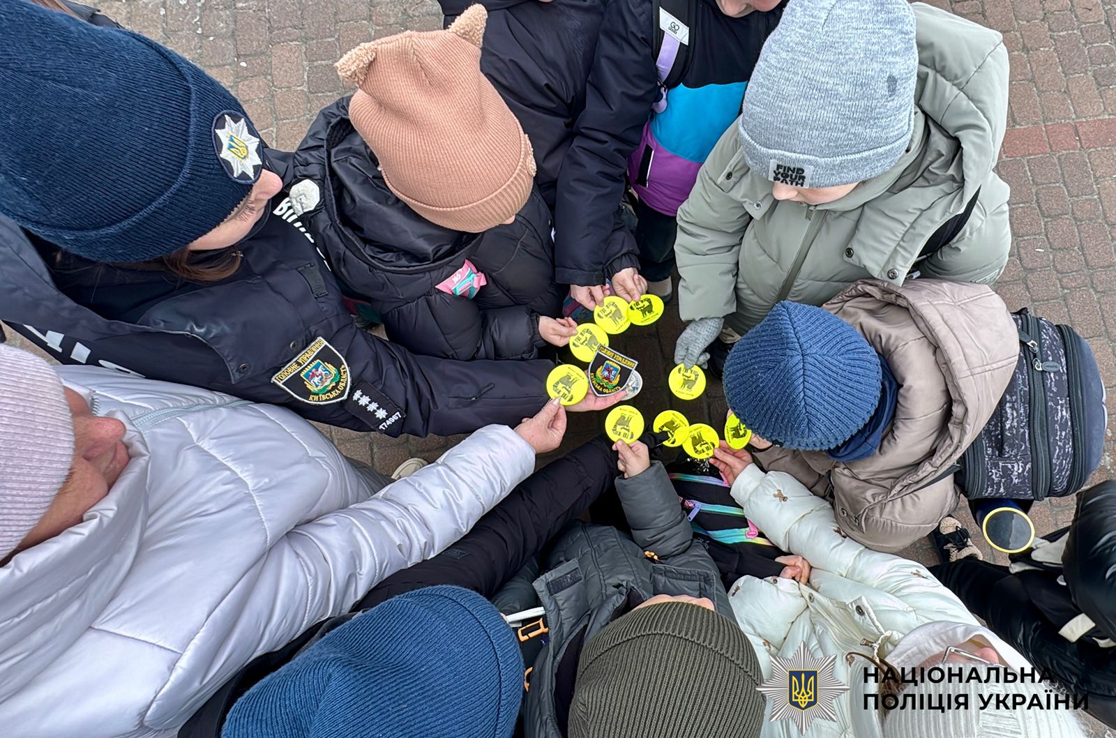 На фотографії зображені діти із світлоповертальними флікерами, які роздали поліцейські київщини, аби вони були помітними у темряві.