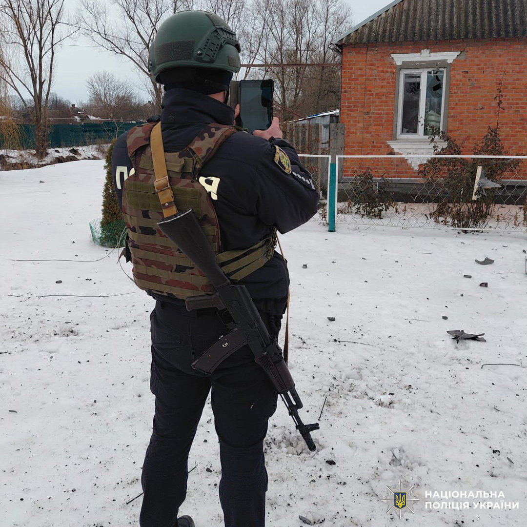 Співробітник Нацполіції у зимовому спорядженні фіксує руйнування будинку з вибитими вікнами.