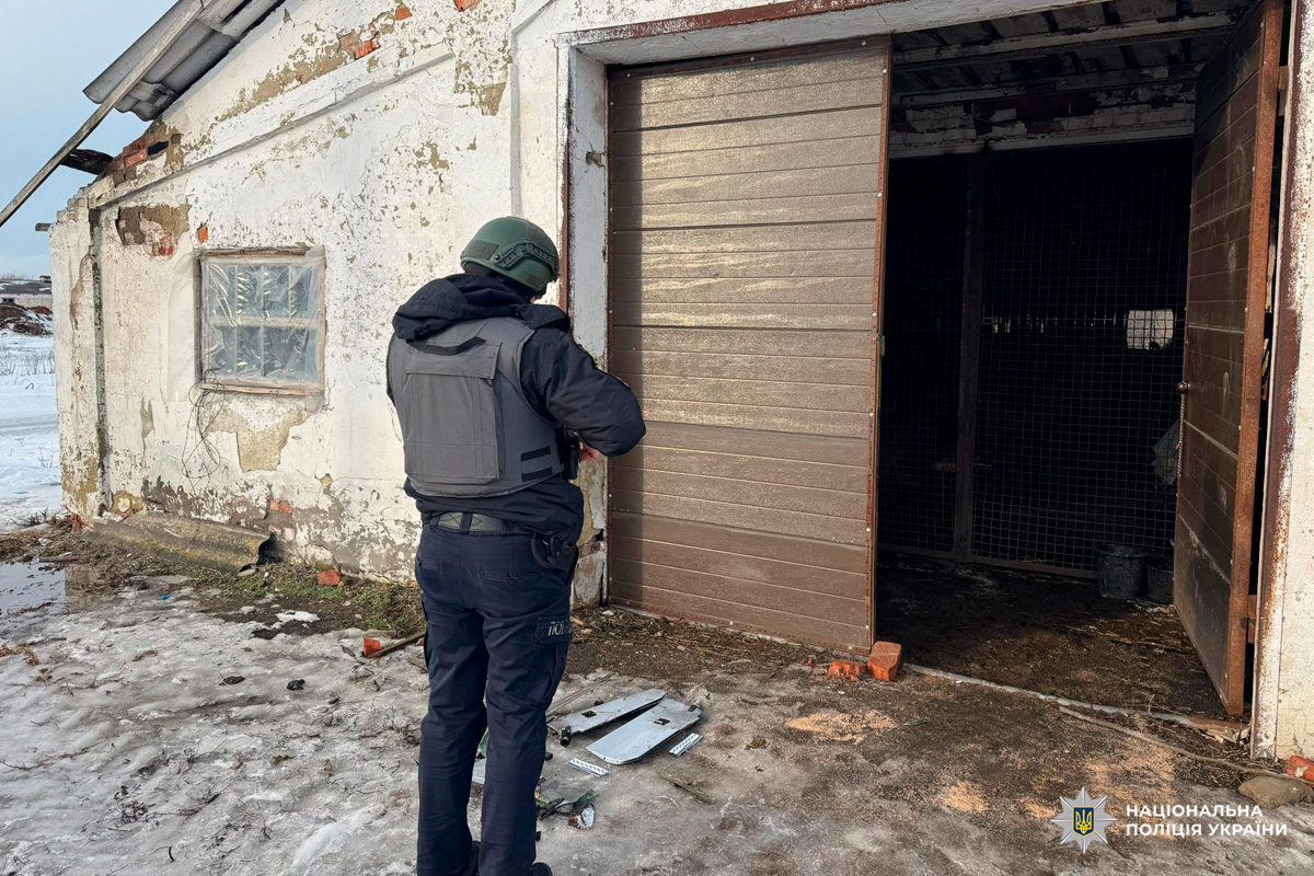 Поліцейський у бронежилеті та касці проводить огляд будівлі з відкритими дверима та слідами руйнувань.