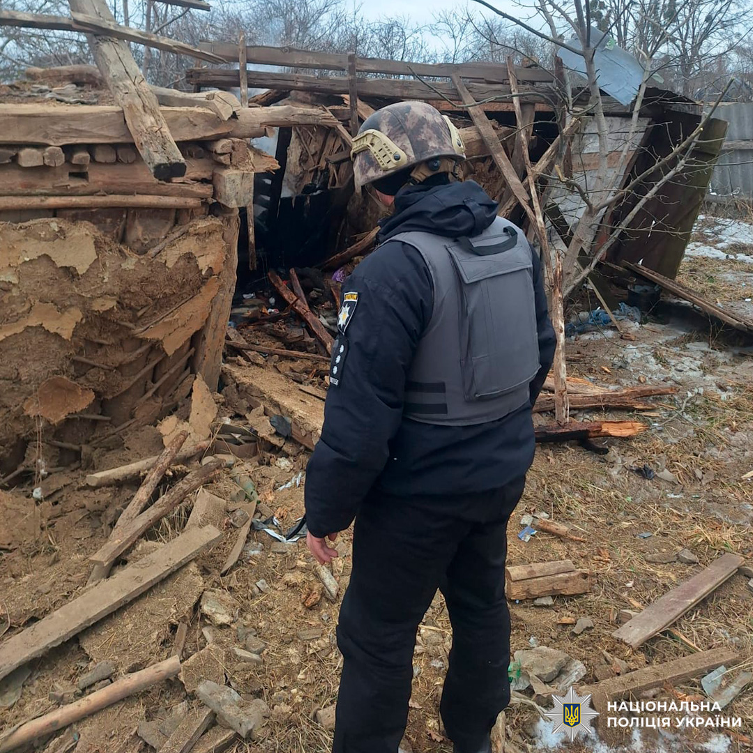 Поліцейський у касці та бронежилеті оглядає пошкоджену дерев’яну споруду, що частково обвалилася.