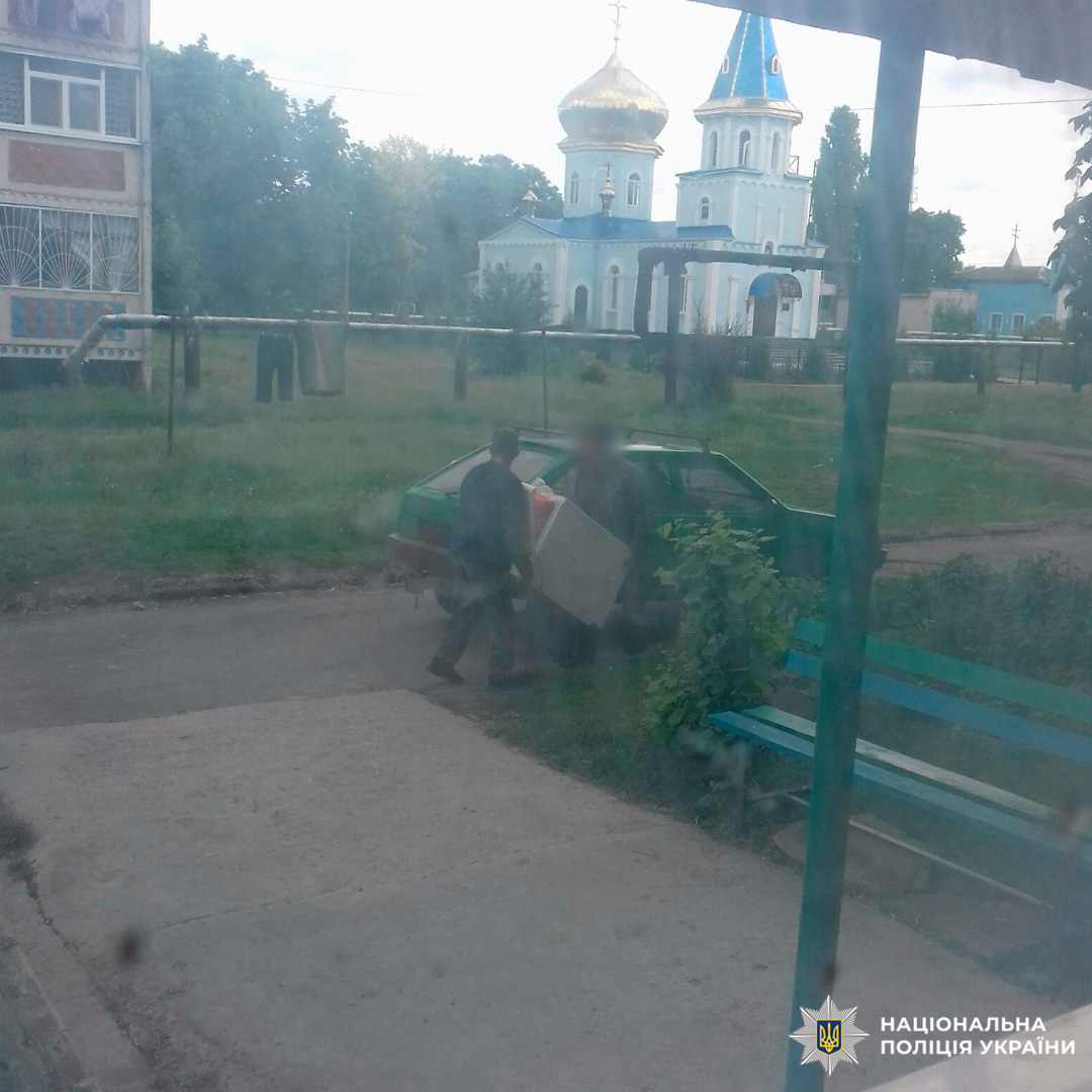 Двоє людей переносять великий предмет із автомобіля біля житлового будинку.