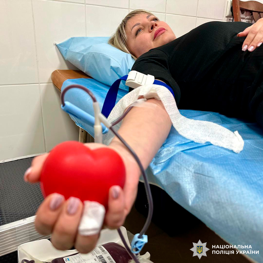 Співробітник Національної поліції України бере участь у донорстві крові, лежачи на медичному ліжку з джгутом на руці.