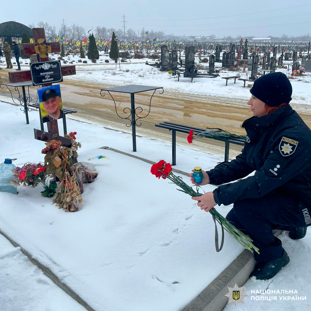 Поліцейський віддає шану герою, запалюючи синьо‑жовту свічку та покладаючи квіти на його засніту могилу.