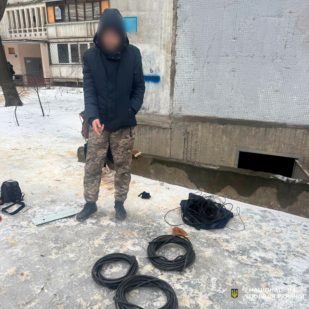 Чоловік у камуфляжних штанах та куртці стоїть на снігу біля кабелів та рюкзака.