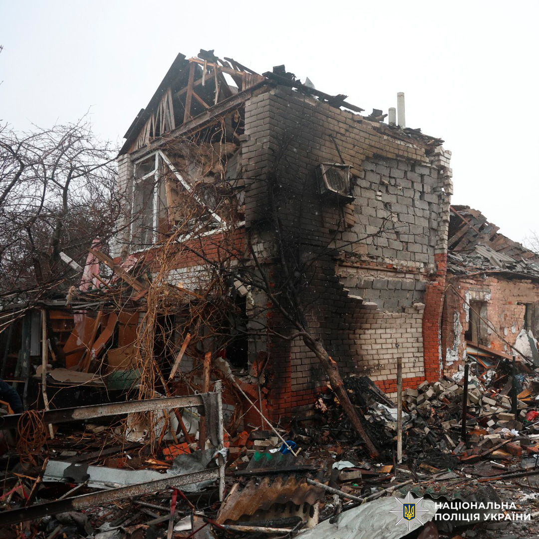 Цегляна споруда з частково обваленим дахом, пошкодженими стінами та слідами пожежі; територія засипана уламками й металевими конструкціями.
