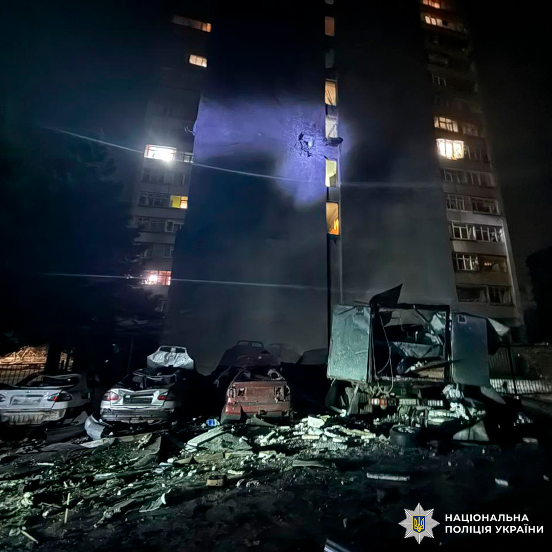 Фасад будинку з видимими слідами удару, поруч уламки та зруйновані транспортні засоби.