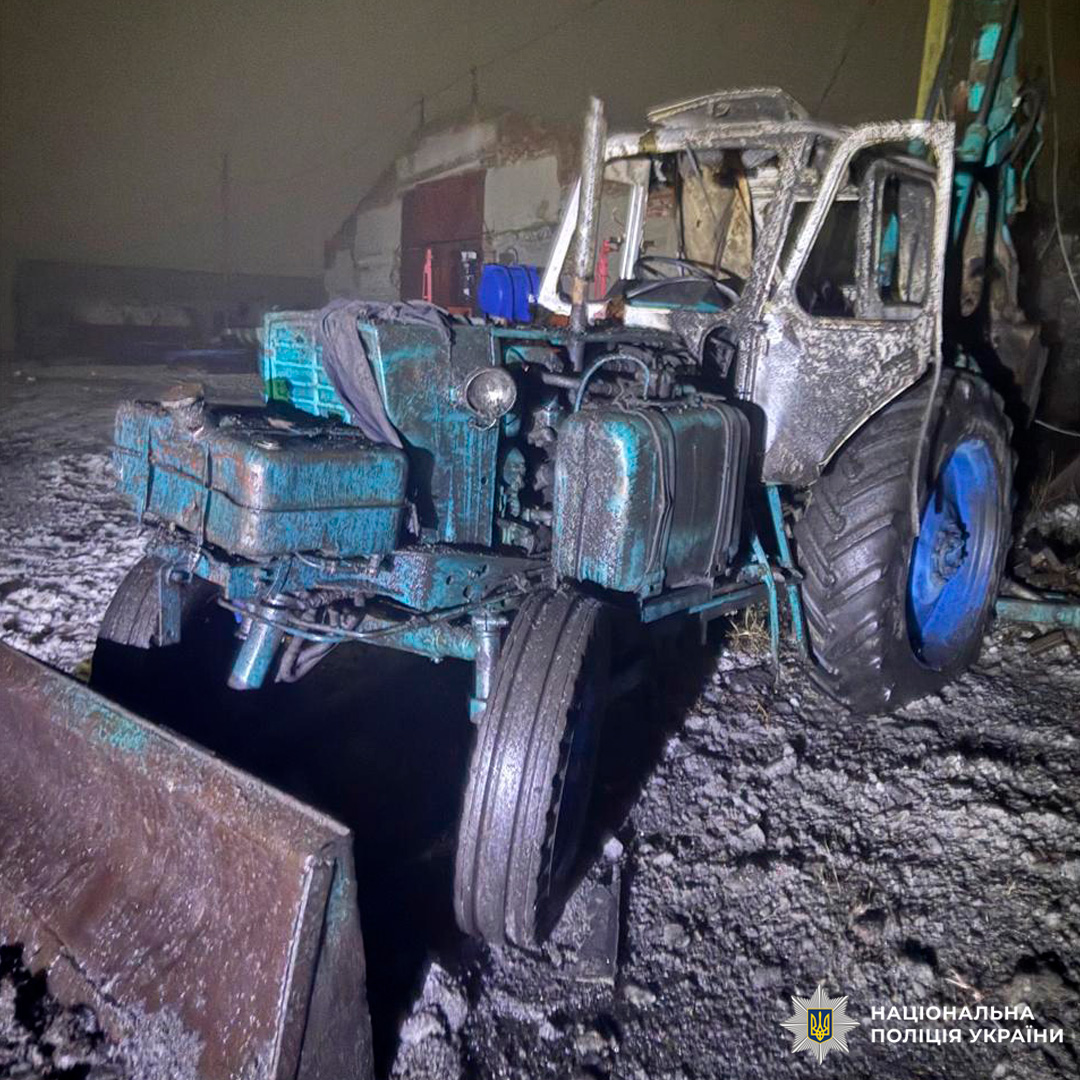 Згорілий трактор у промисловій зоні вночі. Кабіна та двигун мають значні сліди пожежі.