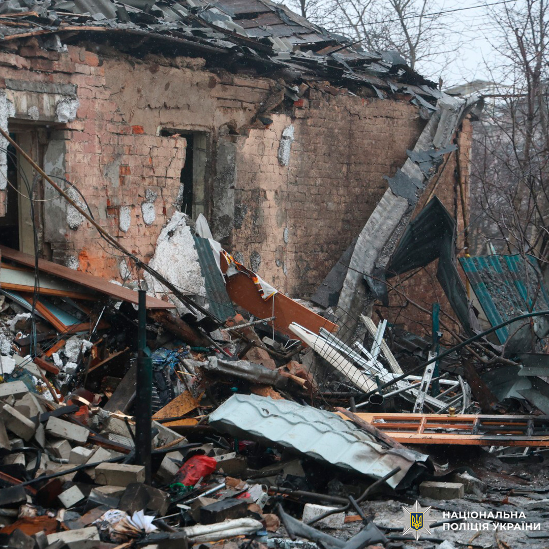 Зруйнована будівля з частково обваленим дахом та тріщинами у стінах. На території видно уламки металу та дерева.